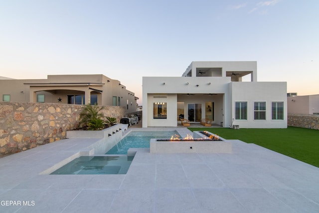 back house at dusk with ceiling fan, a yard, a patio, and an outdoor fire pit