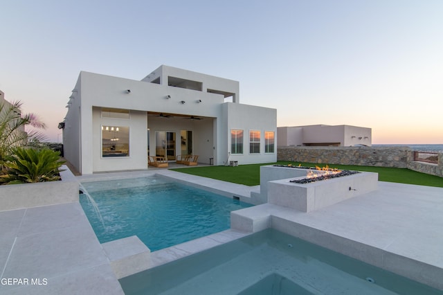 pool at dusk with ceiling fan, pool water feature, a patio, and an outdoor fire pit