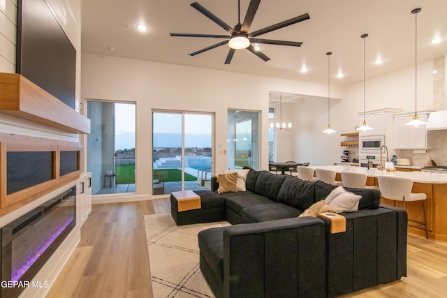 living room with ceiling fan with notable chandelier, a water view, and light hardwood / wood-style flooring