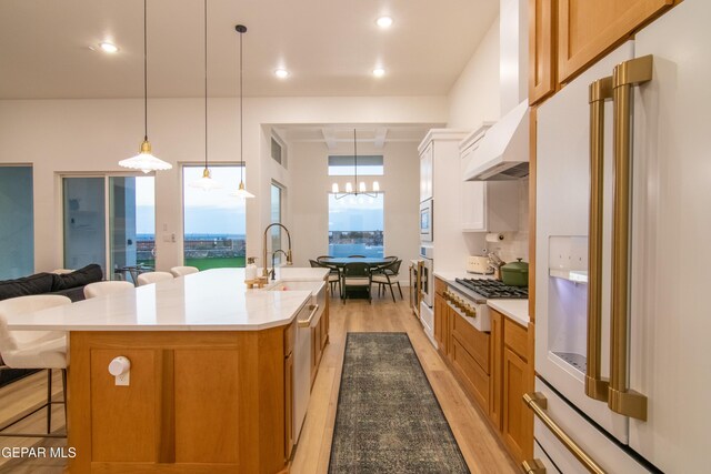 kitchen with custom exhaust hood, high end white fridge, a breakfast bar area, white cabinetry, and a large island