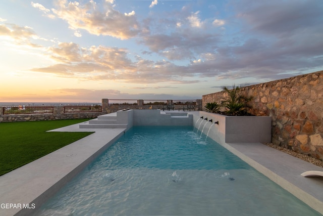 pool at dusk with pool water feature and a yard