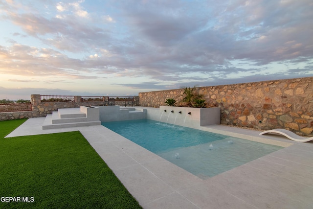 pool at dusk featuring a yard and pool water feature