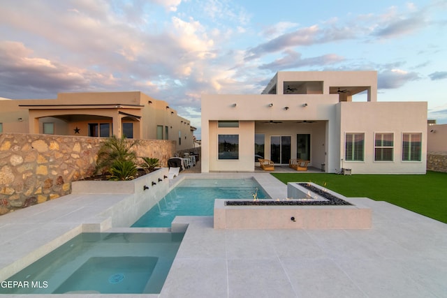 back house at dusk featuring pool water feature, ceiling fan, a pool with hot tub, and a patio