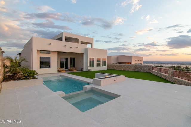 back house at dusk with a yard, a patio area, ceiling fan, and a swimming pool with hot tub