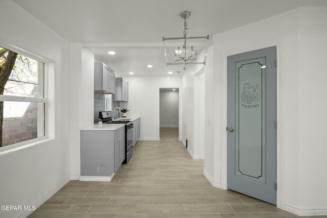 kitchen with tasteful backsplash, gray cabinets, a notable chandelier, and stainless steel gas range