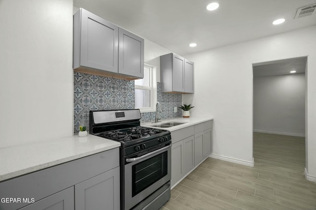 kitchen with sink, backsplash, gray cabinetry, and stainless steel gas range