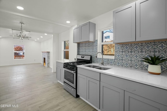 kitchen featuring gray cabinetry, stainless steel gas range oven, sink, decorative light fixtures, and a chandelier