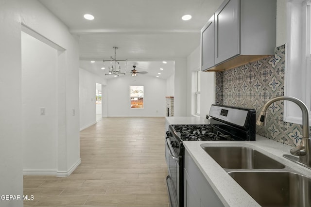 kitchen with stainless steel gas stove, sink, light stone counters, vaulted ceiling, and gray cabinets