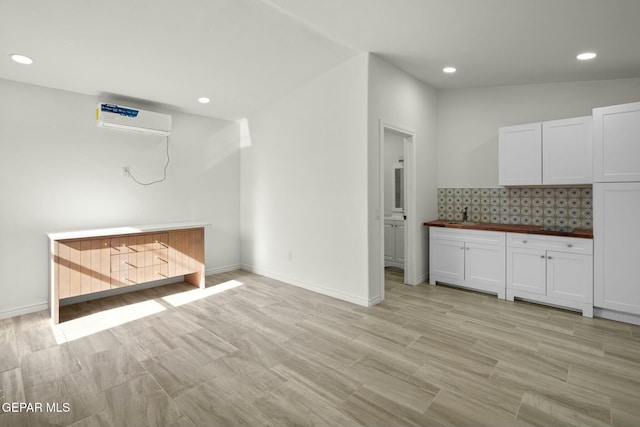 kitchen featuring tasteful backsplash, sink, an AC wall unit, butcher block countertops, and white cabinetry