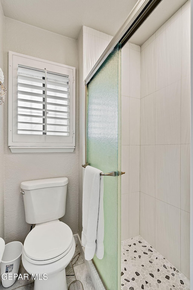 bathroom featuring a shower with shower door and toilet