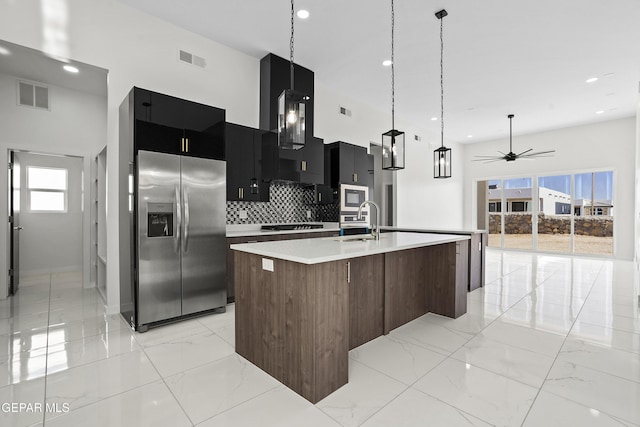 kitchen with sink, a kitchen island with sink, hanging light fixtures, stainless steel appliances, and decorative backsplash