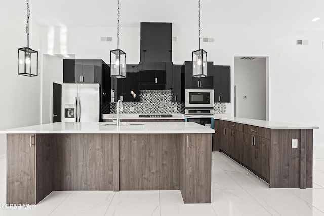 kitchen featuring hanging light fixtures, backsplash, stainless steel appliances, and a center island with sink