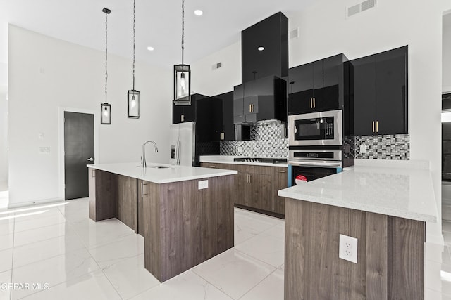 kitchen featuring pendant lighting, stainless steel appliances, a center island with sink, and a high ceiling