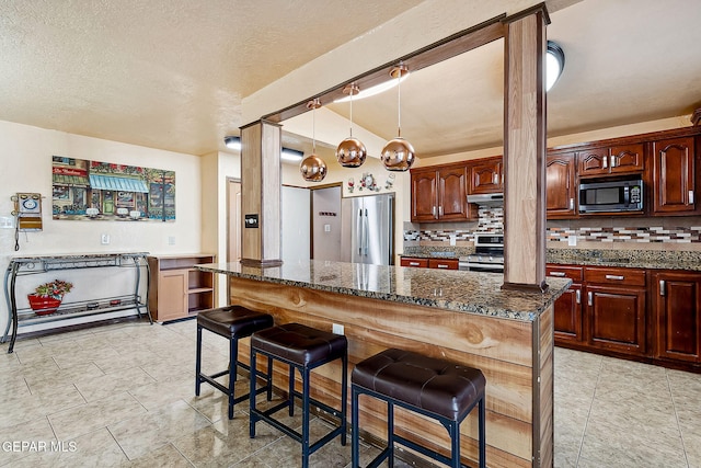 kitchen with a breakfast bar, a center island, dark stone countertops, decorative light fixtures, and stainless steel appliances