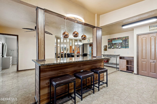 bar with a textured ceiling, decorative light fixtures, ceiling fan, and dark stone counters