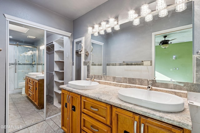 bathroom with vanity, a shower with door, toilet, and ceiling fan