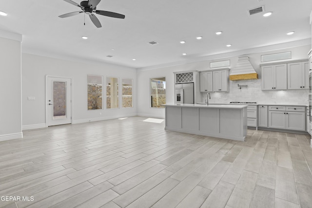 kitchen with ceiling fan, stainless steel fridge, an island with sink, stovetop, and custom range hood