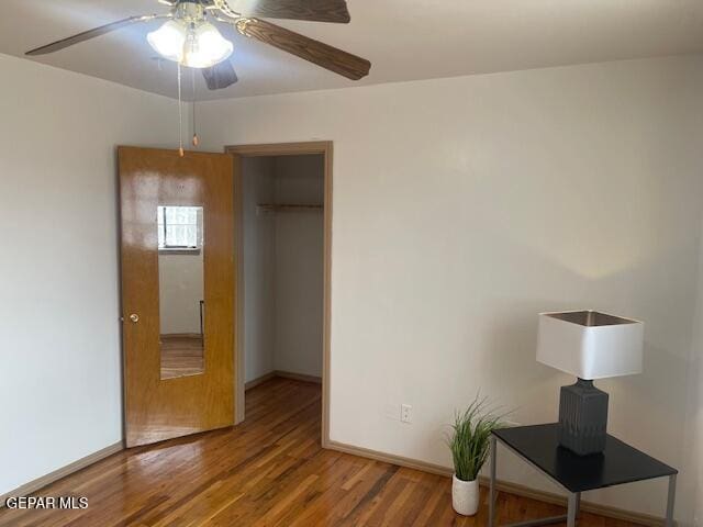 unfurnished bedroom featuring a walk in closet, a closet, hardwood / wood-style floors, and ceiling fan