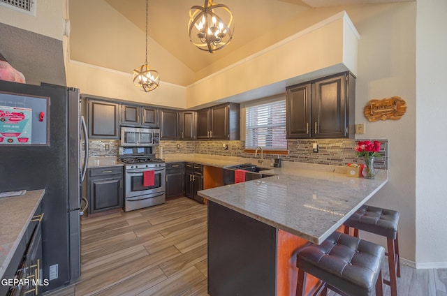 kitchen featuring a peninsula, hanging light fixtures, stainless steel appliances, dark brown cabinets, and a kitchen bar