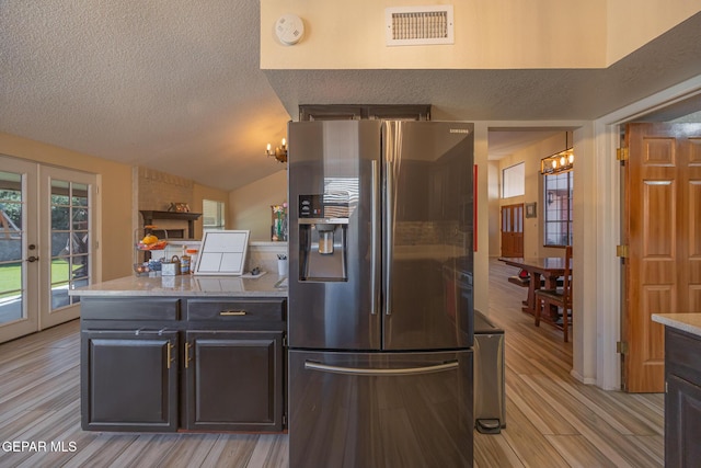 kitchen featuring visible vents, light wood-style flooring, vaulted ceiling, a textured ceiling, and stainless steel refrigerator with ice dispenser