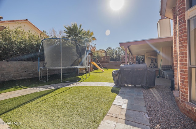 view of yard with a patio, a trampoline, a playground, and fence