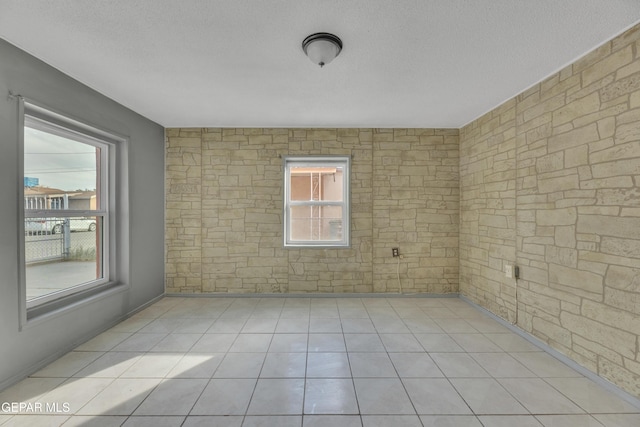 unfurnished room with a healthy amount of sunlight, light tile patterned flooring, and a textured ceiling