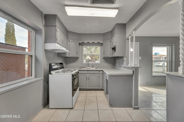 kitchen with white gas stove, gray cabinets, light tile patterned floors, and sink