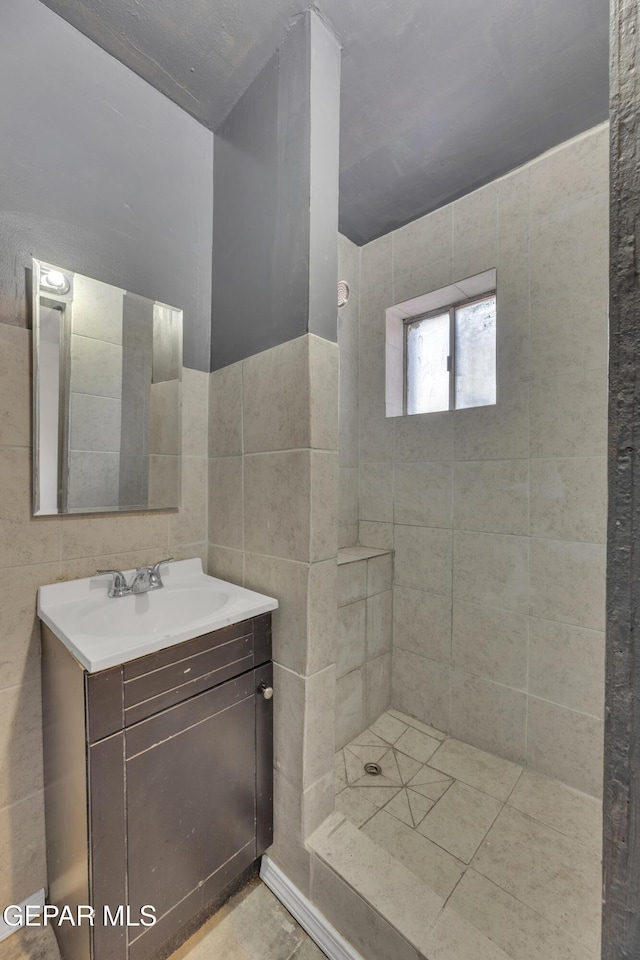 bathroom with tile patterned floors, vanity, a tile shower, and tile walls