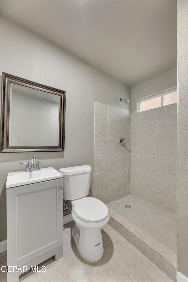 bathroom with a tile shower, vanity, and toilet