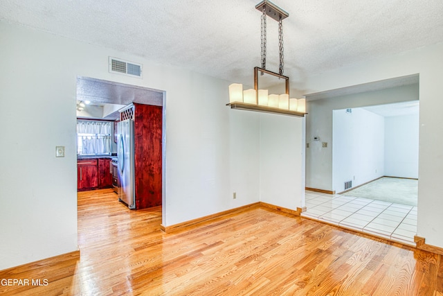 unfurnished room with a textured ceiling and light wood-type flooring