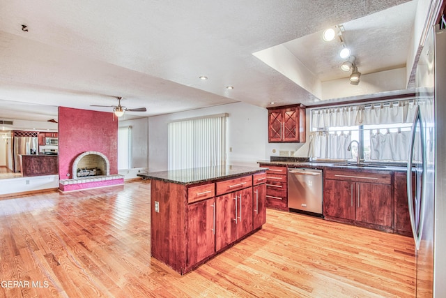 kitchen with a kitchen island, a large fireplace, light hardwood / wood-style floors, stainless steel appliances, and a textured ceiling