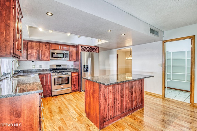 kitchen with appliances with stainless steel finishes, dark stone counters, a center island, a raised ceiling, and a textured ceiling