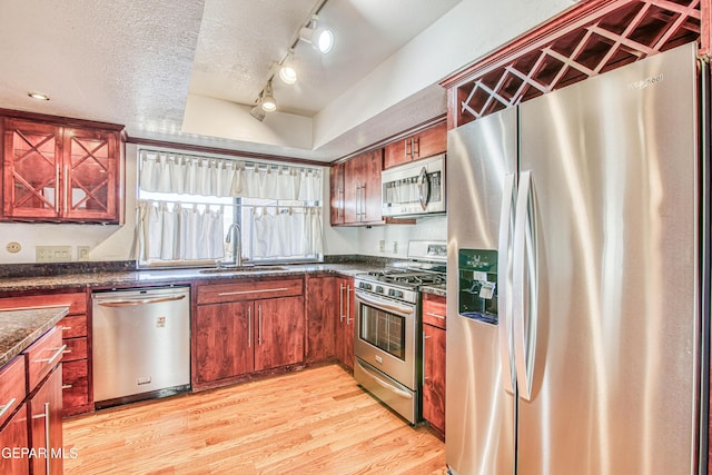 kitchen with sink, appliances with stainless steel finishes, a textured ceiling, dark stone counters, and light wood-type flooring