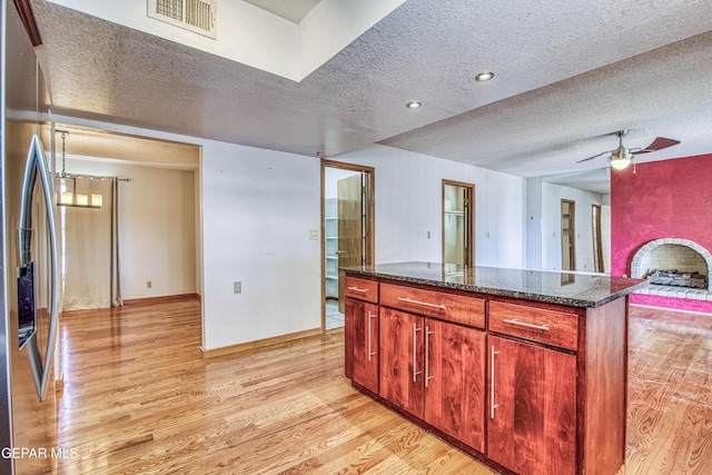 kitchen with dark stone counters, stainless steel fridge with ice dispenser, light hardwood / wood-style flooring, and a textured ceiling