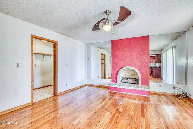 unfurnished living room featuring ceiling fan, a textured ceiling, a fireplace, and light hardwood / wood-style flooring