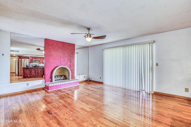 unfurnished living room with hardwood / wood-style flooring, ceiling fan, a fireplace, and a textured ceiling