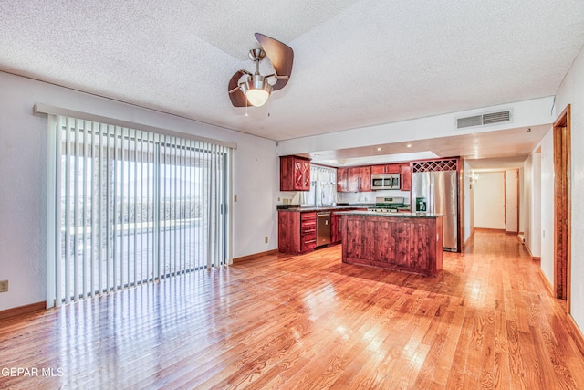 kitchen with sink, stainless steel appliances, a textured ceiling, a kitchen island, and light wood-type flooring