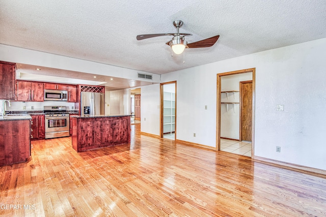 kitchen featuring stainless steel appliances, a center island, a textured ceiling, and light wood-type flooring