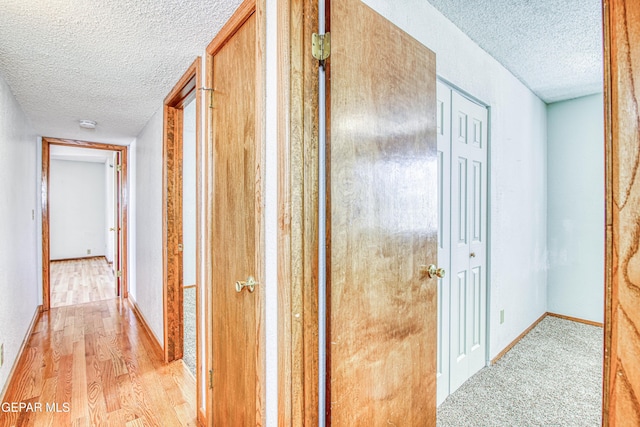 hallway with a textured ceiling and light hardwood / wood-style flooring