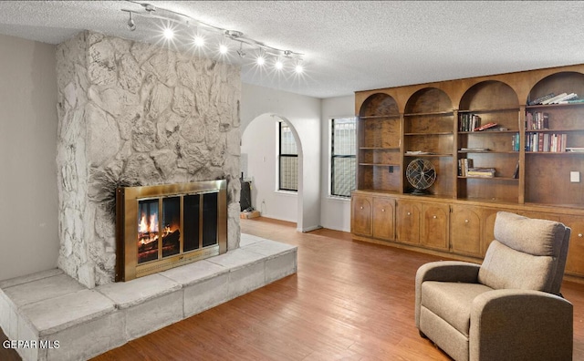 living room with a stone fireplace, light hardwood / wood-style flooring, track lighting, and a textured ceiling