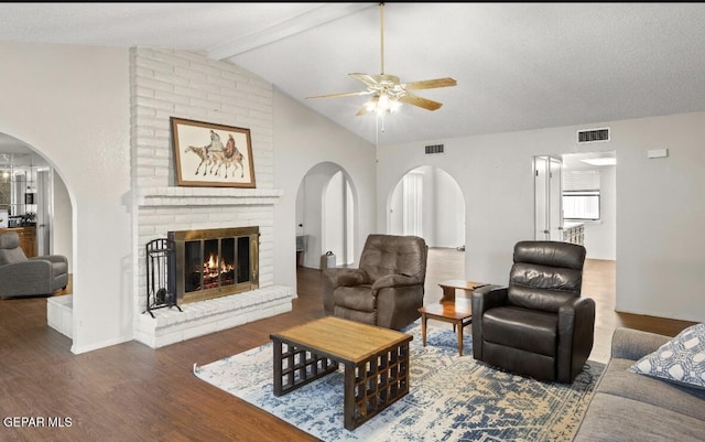 living room with vaulted ceiling with beams, ceiling fan, a textured ceiling, a fireplace, and dark hardwood / wood-style flooring