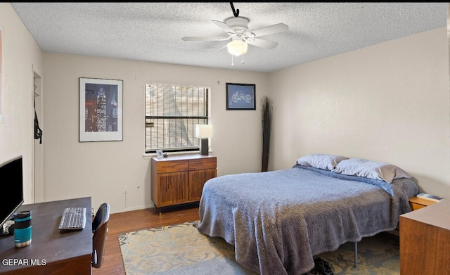 bedroom with ceiling fan, wood-type flooring, and a textured ceiling