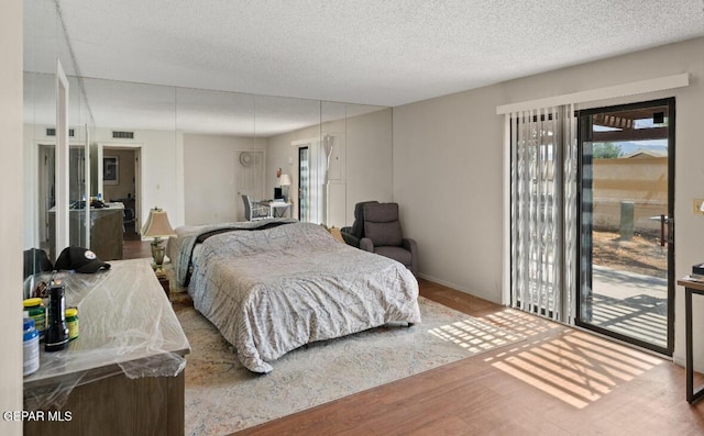 bedroom with wood-type flooring, a textured ceiling, and access to outside