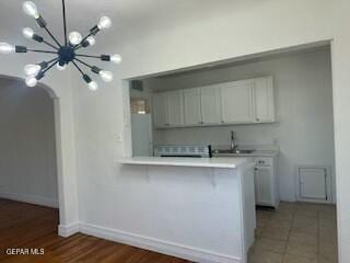 kitchen with white cabinets, a notable chandelier, kitchen peninsula, and sink