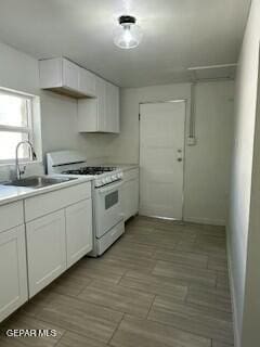 kitchen featuring white range with gas stovetop, white cabinetry, and sink