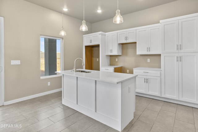 kitchen featuring hanging light fixtures, an island with sink, sink, and white cabinets