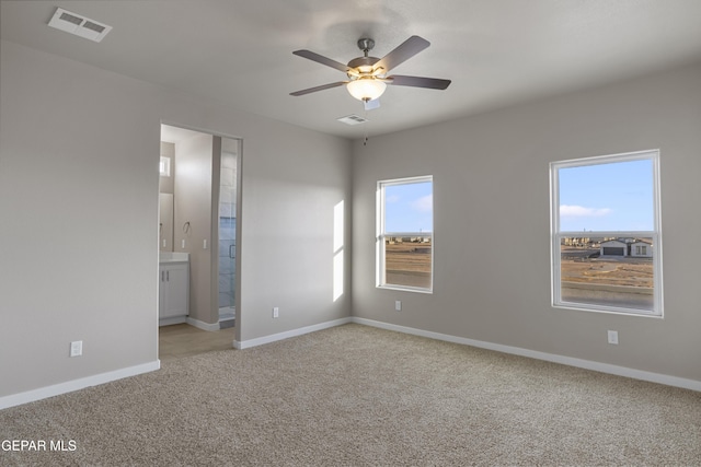 unfurnished bedroom featuring ceiling fan, light colored carpet, and ensuite bath