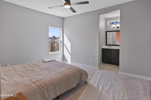 bedroom with ceiling fan, sink, light colored carpet, and ensuite bath