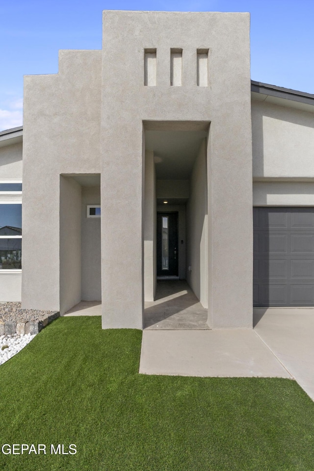 view of exterior entry featuring a garage and a lawn