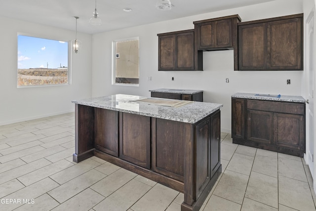 kitchen with light stone counters, pendant lighting, and dark brown cabinetry